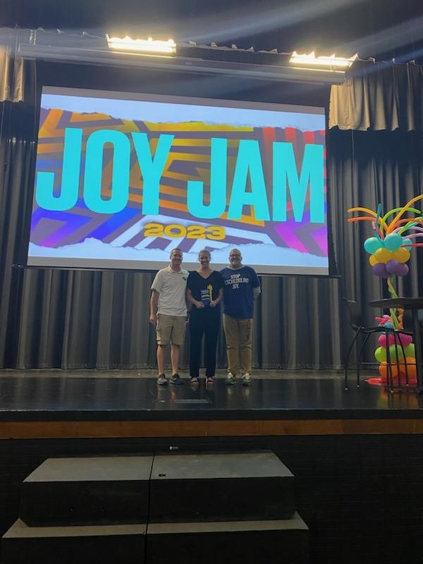 George Philhower, Katie Lash, and Jeremy Duncan on stage in from of the Joy Jam background. 